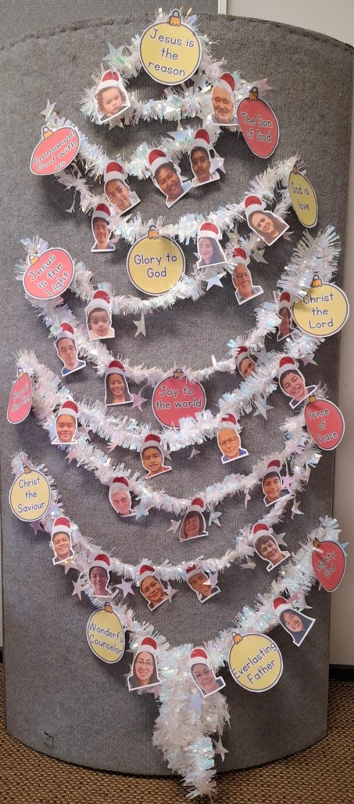 A tinsel Christmas tree hung with paper baubles, each carrying a photograph of a church member's face and a name for Jesus.