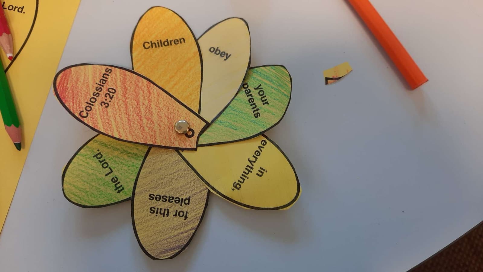 A paper flower coloured in by hand, its petals reading Children obey your parents in everything, for this pleases the Lord. Colossians 3:20.