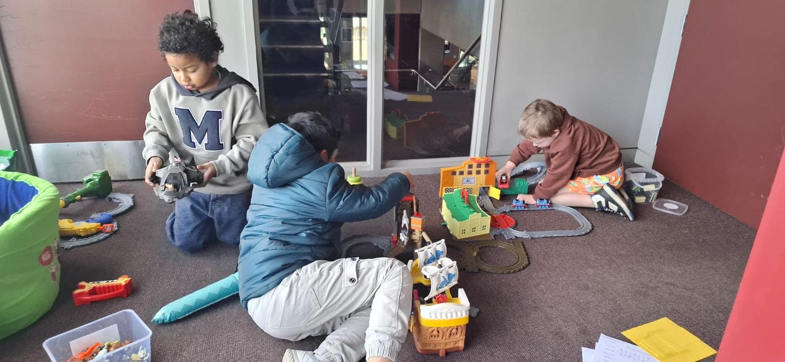 Three young children playing with toy cars and a train set on the floor.
